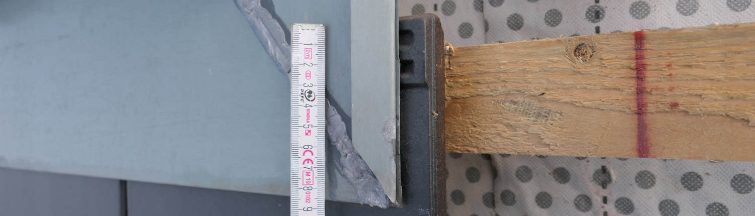 Detailprüfung am Steildach-Anschluss Nahaufnahme einer präzisen Messung mittels Gliedermassstab an einer Metallabdeckung im Übergangsbereich einer Dachkonstruktion zur Beweissicherung.