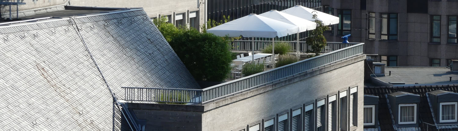 Dachterrasse auf modernem Bürogebäude Weitwinkelaufnahme eines Gebäudekomplexes mit Fokus auf eine Dachterrasse, die mit weißen Sonnenschirmen und Sitzgelegenheiten ausgestattet ist.